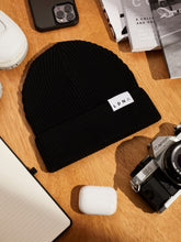 Load image into Gallery viewer, LDNA London black fisherman style beanie with Canon camera, iPhone, magazines and LDNA lined paper notebook on wooden table.